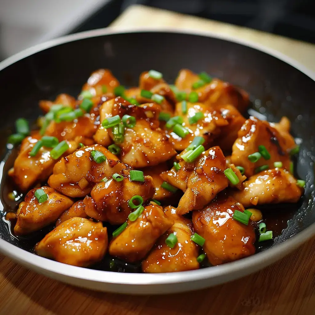 Un délicieux plat de poulet dans une sauce gourmande et sucrée, agrémenté de ciboulette, servi dans un bol noir.