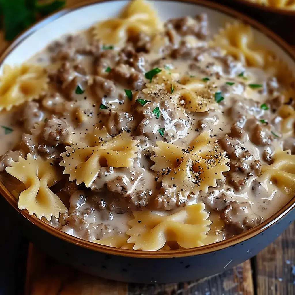 Un bol de farfalle nappées d'une sauce au parmesan et viande hachée, parsemées de poivre et persil frais.