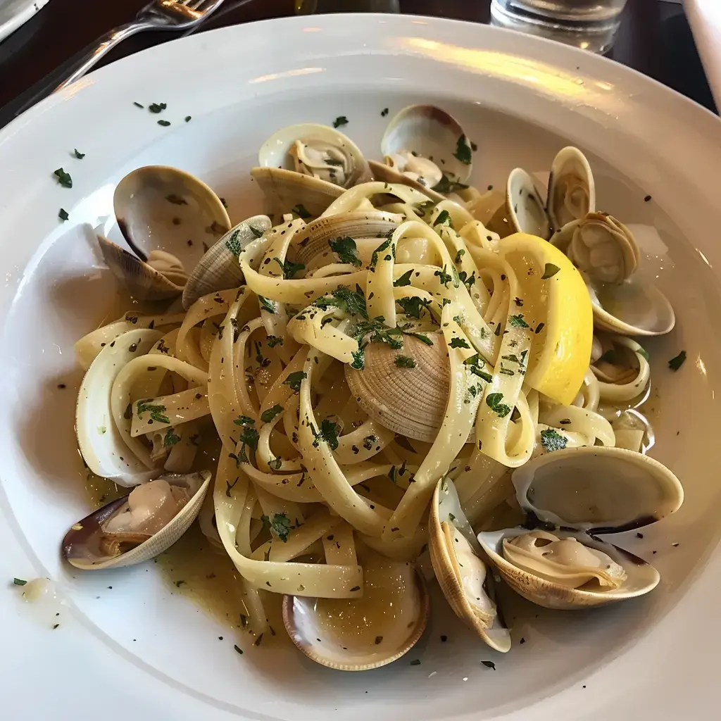 Un plat de pâtes aux palourdes, garni de citron et de persil, servi dans une assiette blanche.