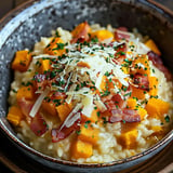 Un délicieux risotto servi dans un bol, garni de morceaux de courge, de lardons croustillants et de fromage râpé.