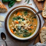 Bol de soupe crémeuse avec des haricots blancs, des légumes, et une garniture de fromage râpé, accompagné de pain rustique.