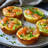 Tartelettes garnies de saumon fumé, poireaux et herbes fraîches, joliment servies sur une assiette.