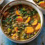 Bol en céramique rempli d’une soupe aux lentilles et fanes de carottes.