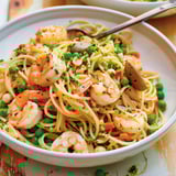 Plat de pâtes aux fruits de mer, avec légumes colorés comme tomates, pois et carottes.