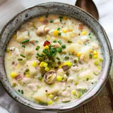 Un bol rempli d'une soupe crémeuse aux palourdes, poisson et légumes, garni d'herbes fraîches servi sur une table chaleureuse.
