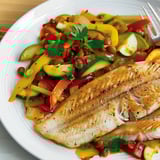 Filet de dorade servi avec des légumes colorés dans une poêle.