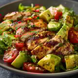 Une assiette fraîche avec poulet grillé, avocat, tomates et fines herbes.