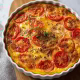 Une quiche délicate et légère, sans pâte avec thon et tomate, servie dans un plat rond.