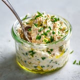 Une cuillère plonge dans une assiette de thon crémeux, décorée avec des herbes fraîches.