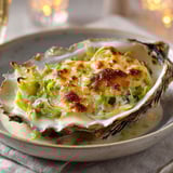 Plat de huîtres gratinées avec poireaux, accompagné d'une bouteille de vin blanc.