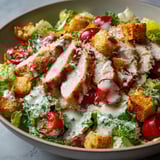 Un plat de salade César avec morceaux de noix de veau, légumes frais et croûtons dorés, servi dans une assiette.