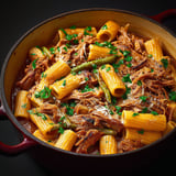 Porc braisé servi avec rigatonis et oignons dorés, dans un grand bol.